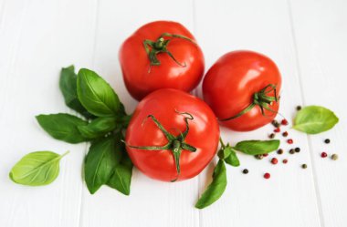 Beyaz ahşap bir masa üzerinde yeşil fesleğen ile taze domates