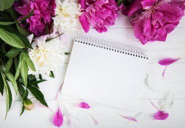 Beyaz ahşap zemin üzerinde peonies not defteriyle