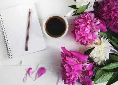 Beyaz ahşap zemin üzerinde peonies ve kahve ile not defteri