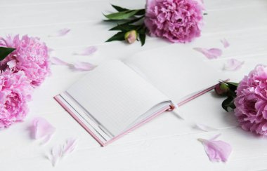 Beyaz ahşap zemin üzerinde peonies not defteriyle