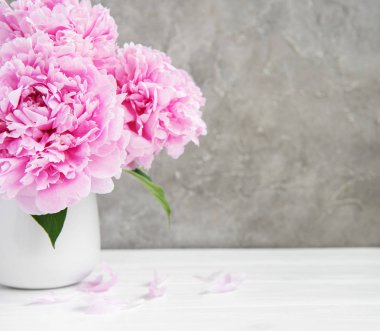 Beyaz ahşap bir masa üzerinde pembe şakayık çiçekli vazo