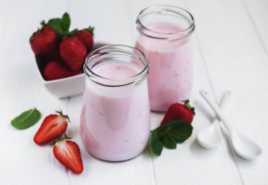 Kavanoz bir beyaz tahta masada çilekli yoğurt ile