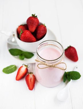 Beyaz ahşap bir masa üzerinde çilekli yoğurt ile jar