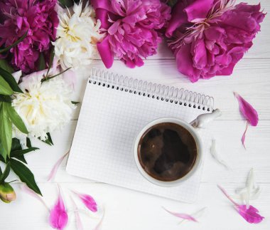 Beyaz ahşap zemin üzerinde peonies ve kahve ile not defteri