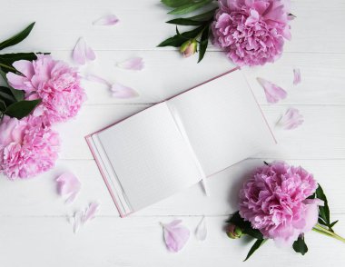 Beyaz ahşap zemin üzerinde peonies not defteriyle