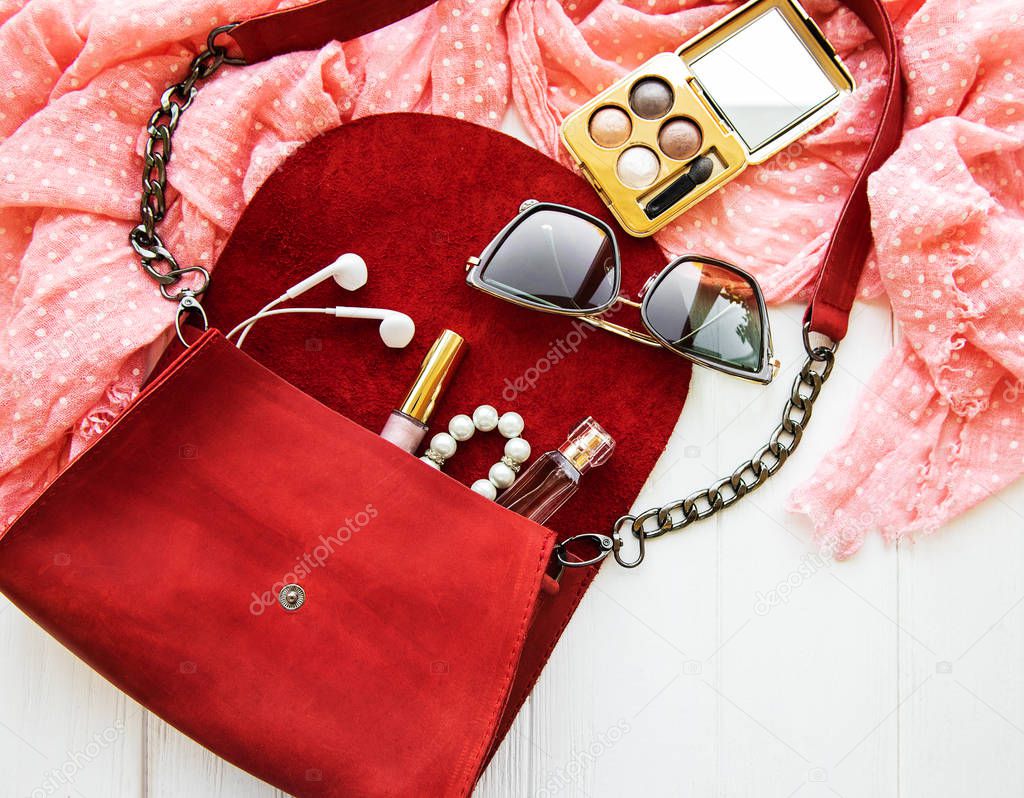 Red leather bag with accessories on a white wooden table