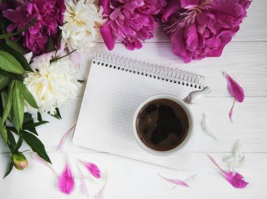 Beyaz ahşap zemin üzerinde peonies ve kahve ile not defteri