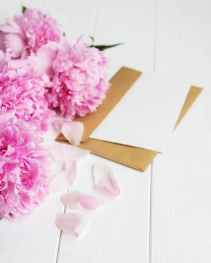davetiye, zanaat zarf ve pembe şakayık çiçekleri Beyaz ahşap bir masa üzerinde
