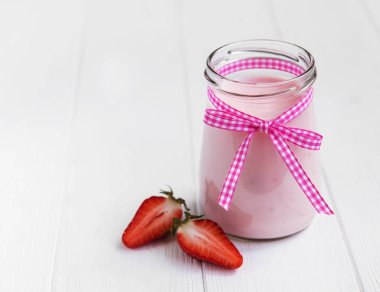 Beyaz ahşap bir masa üzerinde çilekli yoğurt ile jar