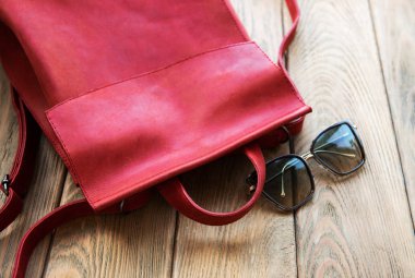 Kırmızı deri sırt çantası ve eski ahşap bir masa üzerinde gözlük