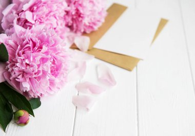 davetiye, zanaat zarf ve pembe şakayık çiçekleri Beyaz ahşap bir masa üzerinde