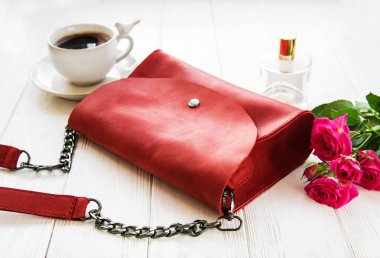 Ahşap arka plan üzerinde kırmızı deri çanta ve pembe güller