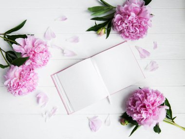Beyaz ahşap zemin üzerinde peonies not defteriyle
