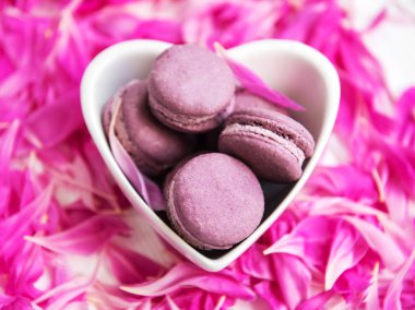 Beyaz ahşap bir masa üzerinde macarons ile pembe şakayık yaprakları