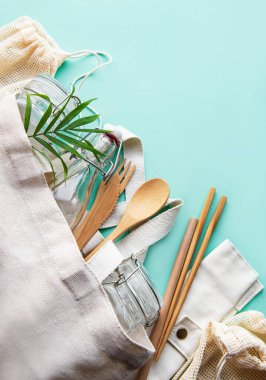 Sıfır atık, plastiksiz ve çevre dostu yaşam tarzı. Pamuklu örgü çanta, cam şişe, kavanoz ve yeşil arka planda bambu çatal bıçak takımı. Düz yatıyordu. 