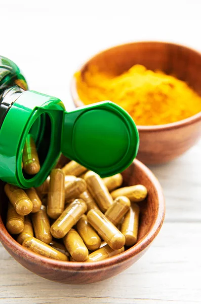 Turmeric powder and turmeric capsules on white wooden background