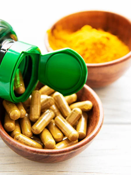 Turmeric powder and turmeric capsules on white wooden background