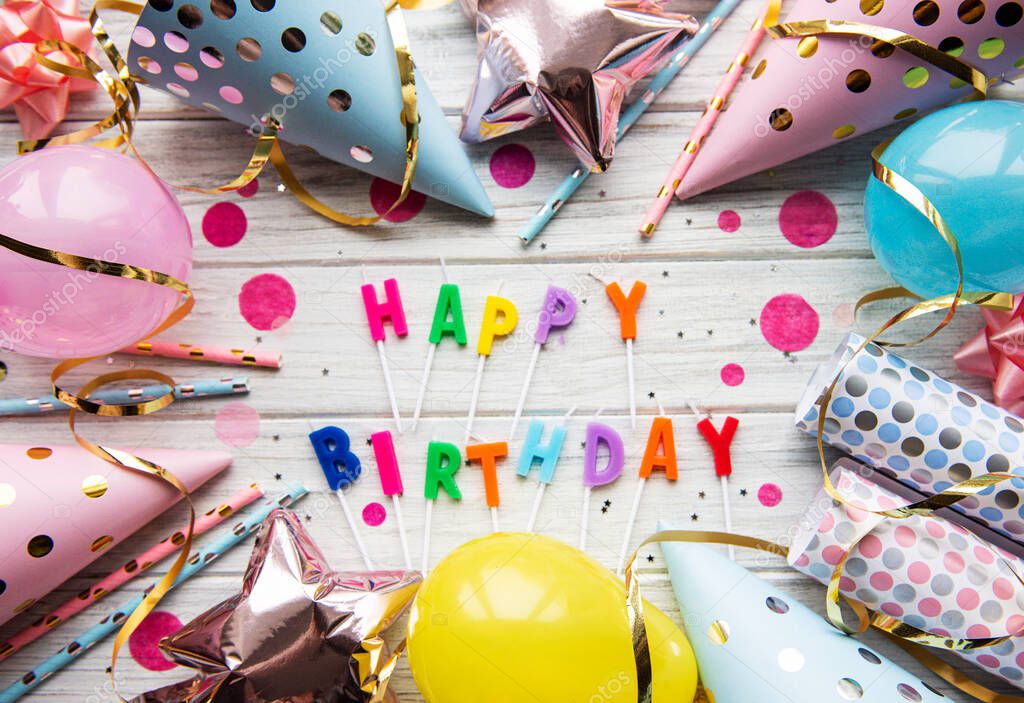 Text Happy Birthday by candle  letters with birthday asseccories, candles and confetti  on pwhite wooden background