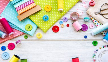 Beyaz arka planda aksesuar ve kumaş dikmek. Dikiş iplikleri, iğneler, iğneler, kumaşlar, düğmeler ve dikiş santimetresi. Üst manzara, düz uzanma.
