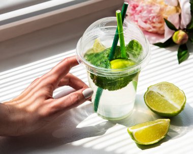 Mojito kokteyli, pencerenin önündeki kadın ellerinde ve bir buket şakayık.