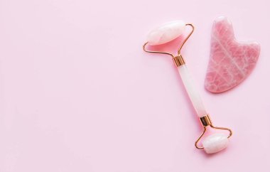 Güzellik masajı terapisi için yeşim yüz silindiri. Pembe arka planda düz uzandı