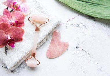 Havlu ve orkide çiçekleriyle güzellik masajı için yeşim yüz silindiri. Mermer zemin üzerinde düz yatıyordu