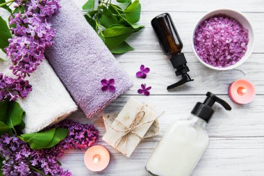 Leylak çiçekli spa seti. Kasede deniz tuzu, aroma yağı şişeleri ve ahşap arka planda mumlar.. 