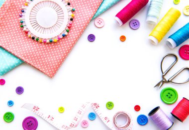 Beyaz arka planda aksesuar ve kumaş dikmek. Dikiş iplikleri, iğneler, iğneler, kumaşlar, düğmeler ve dikiş santimetresi. Üst manzara, düz uzanma.