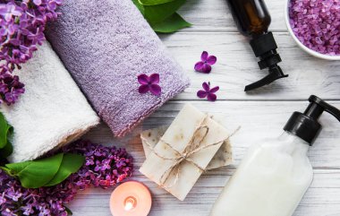 Leylak çiçekli spa seti. Kasede deniz tuzu, aroma yağı şişeleri ve ahşap arka planda mumlar.. 