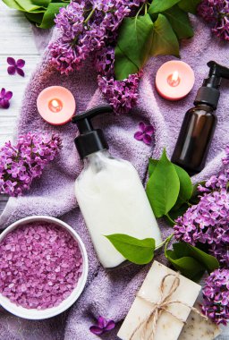 Leylak çiçekli spa seti. Kasede deniz tuzu, aroma yağı şişeleri ve ahşap arka planda mumlar.. 