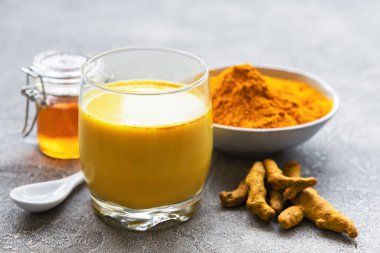 Sarı zerdeçal latte. Tarçınlı altın süt, zerdeçal, zencefil ve bal gri beton arka planda.