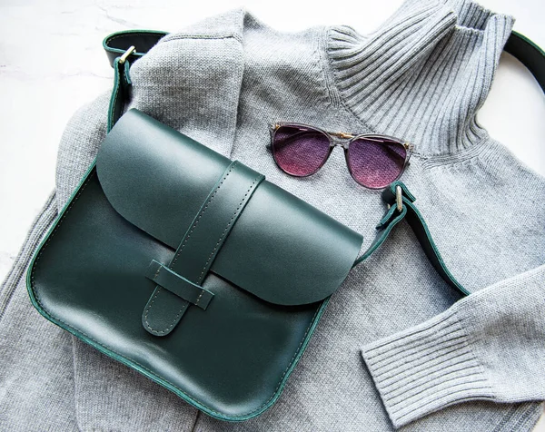 Green leather women bag, grey knitted sweater,  top view, flat lay. Fashionable women\'s accessories. Autumn Fashion Concept.