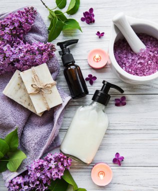 Leylak çiçekli spa seti. Kasede deniz tuzu, aroma yağı şişeleri ve ahşap arka planda mumlar.. 