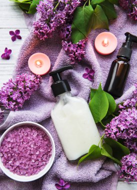 Leylak çiçekli spa seti. Kasede deniz tuzu, aroma yağı şişeleri ve ahşap arka planda mumlar.. 
