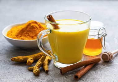 Sarı zerdeçal latte. Tarçınlı altın süt, zerdeçal, zencefil ve bal gri beton arka planda.