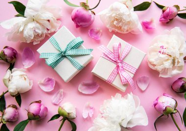 Pembe pastel arka planda şölen kompozisyonu: şakayık çiçekleri, hediye kutuları. Üst görünüm, alanı kopyala.