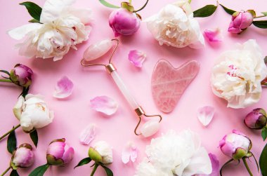 Güzel yüz masajı terapisi ve pembe şakayıklar için yeşim yüz silindiri. Pembe pastel arka planda düz uzandı
