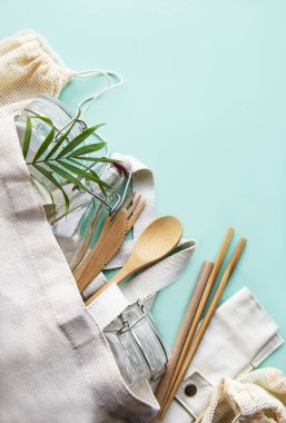 Sıfır atık, plastiksiz ve çevre dostu yaşam tarzı. Pamuklu örgü çanta, cam şişe, kavanoz ve yeşil arka planda bambu çatal bıçak takımı. Düz yatıyordu. 