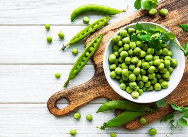 Masanın üstünde taze kabuklu yeşil bezelyeler var, üst ya da düz.