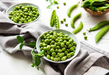 Masanın üstünde taze kabuklu yeşil bezelyeler var, üst ya da düz.