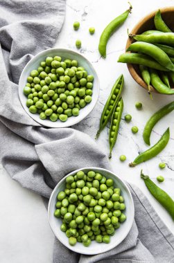Masanın üstünde taze kabuklu yeşil bezelyeler var, üst ya da düz.
