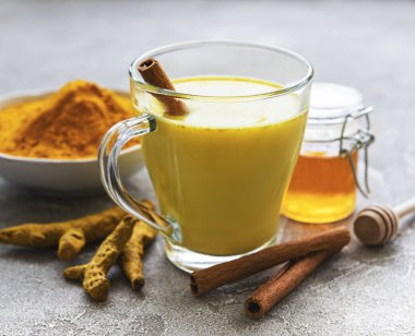 Sarı zerdeçal latte. Tarçınlı altın süt, zerdeçal, zencefil ve bal gri beton arka planda.
