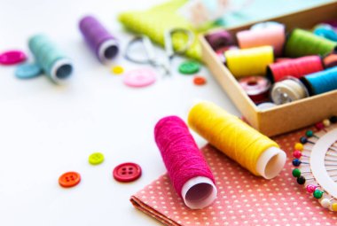 Beyaz arka planda aksesuar ve kumaş dikmek. Dikiş iplikleri, iğneler, iğneler, kumaşlar, düğmeler ve dikiş santimetresi. Üst manzara, düz uzanma.