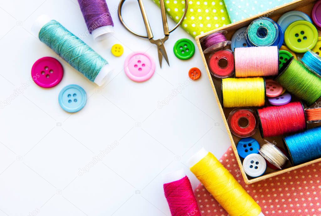 Sewing accessories and fabric on a white background. Sewing threads, needles, pins, fabric, buttons and sewing centimeter. Top view, flat lay.
