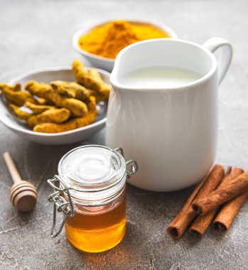 Zerdeçal latte için malzemeler. Zemin zerdeçal, sokağa çıkma yasağı kökü, tarçın, gri beton arka planda bir sürahi süt. Üst görünüm, alanı kopyala