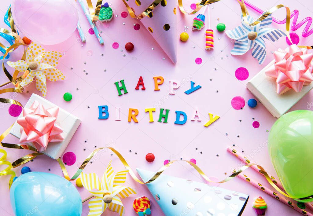 Text Happy Birthday by wooden  letters with birthday asseccories, candles and confetti  on pink background