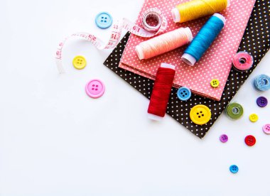 Beyaz arka planda aksesuar ve kumaş dikmek. Dikiş iplikleri, iğneler, iğneler, kumaşlar, düğmeler ve dikiş santimetresi. Üst manzara, düz uzanma.