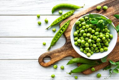 Masanın üstünde taze kabuklu yeşil bezelyeler var, üst ya da düz.