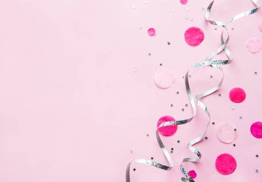 Pembe arka planda gümüş kurdeleler ve pembe konfetilerle şenlikli minimal düz konum kompozisyonu. Düzlük, doğum günü ya da parti konsepti