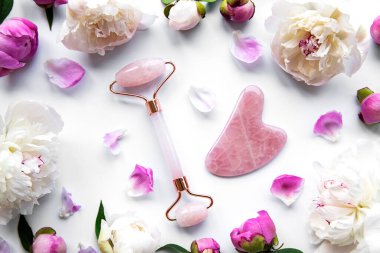 Güzel yüz masajı terapisi ve pembe şakayıklar için yeşim yüz silindiri. Beyaz arkaplan üzerinde düz uzandı